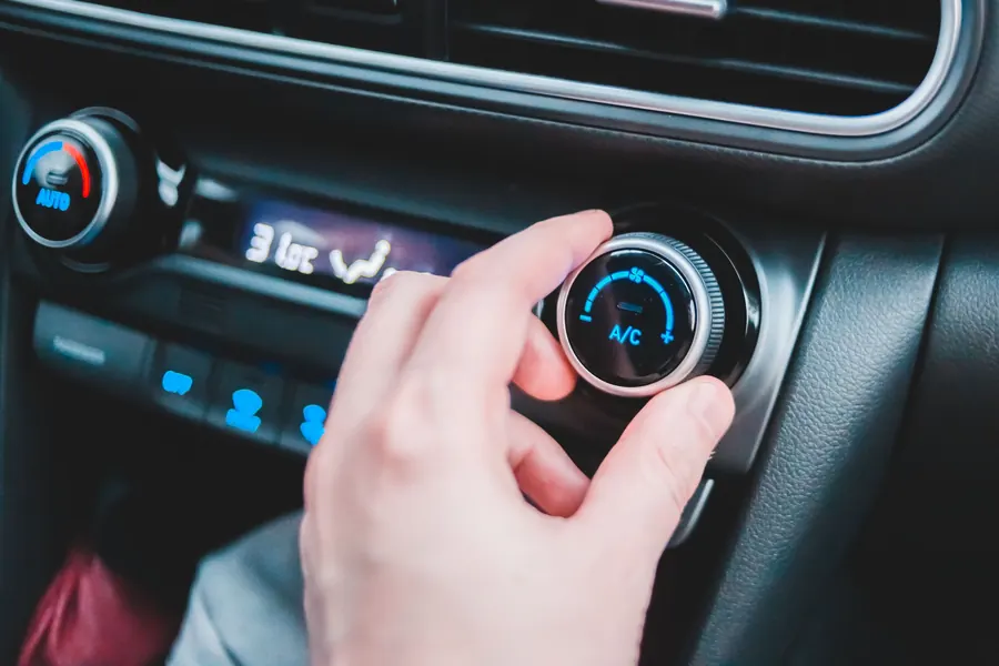 A hand turning a car's A/C climate control knob