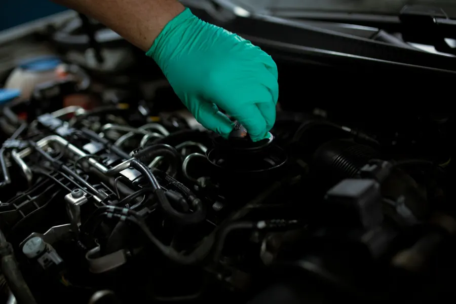 A gloved hand opening the oil filler cap on a car engine