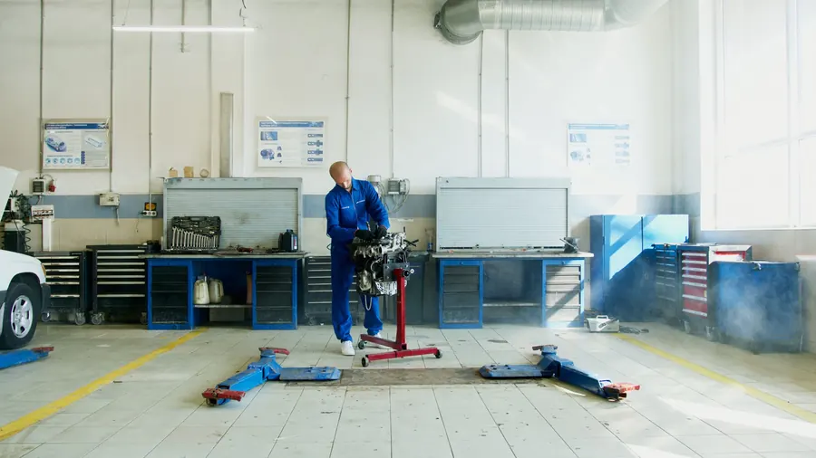 A bright, tidy repair bay with tool chests along the wall and a technician working on an engine on a stand