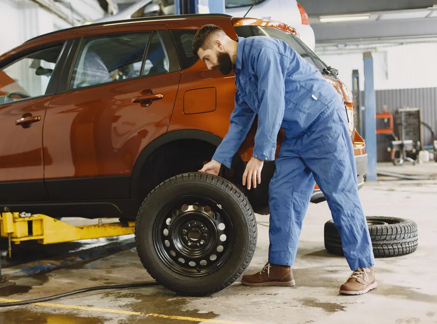A mechanic fitting a wheel onto an SUV on a lift