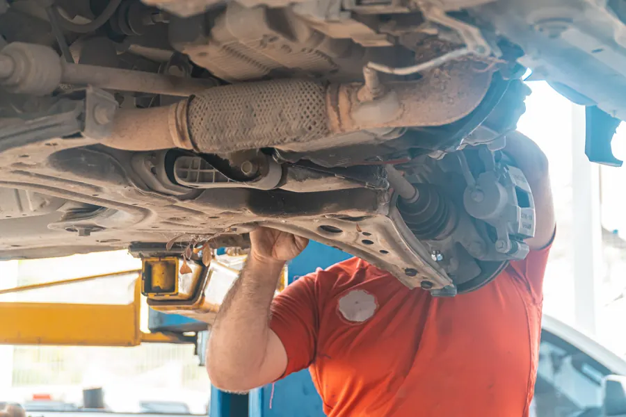 A mechanic under a raised car checking the suspension